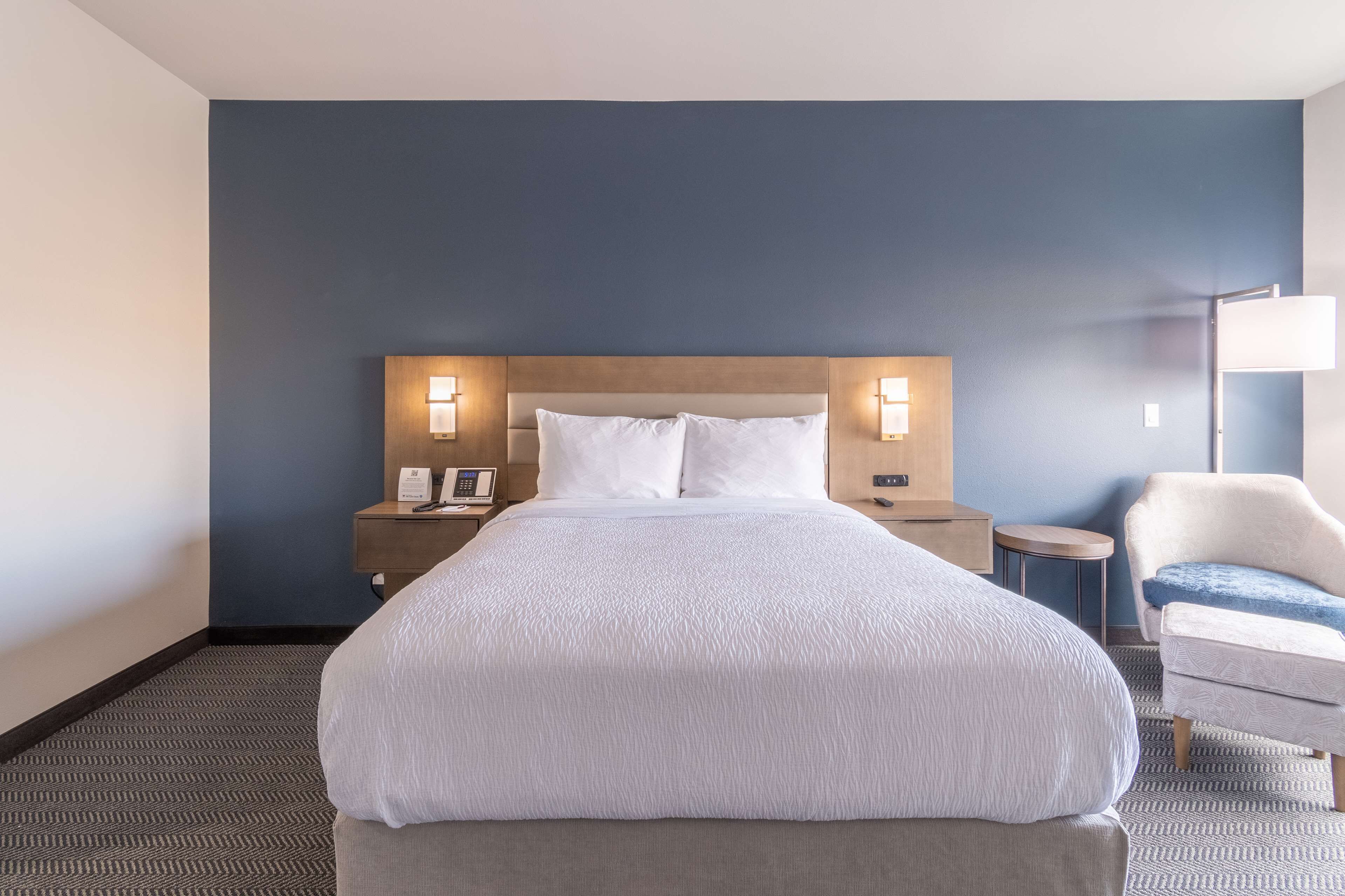 A hotel room with a large bed, two bedside tables with lamps, a chair, and a small round table.