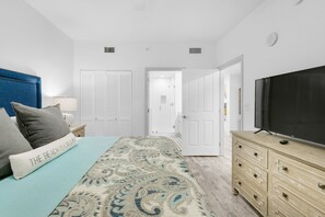 A bedroom with a bed, a TV, a dresser, and a door leading to a bathroom.