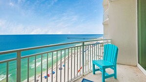 A balcony with a turquoise chair, overlooking a beach with people and umbrellas.