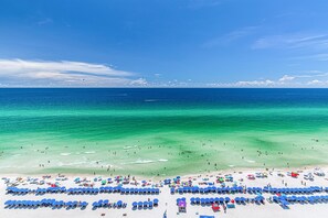 A beach with rows of blue umbrellas and sun loungers, clear turquoise water, and a clear sky.