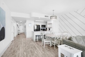 A modern kitchen with white cabinetry, a central island, and a dining area with white chairs.