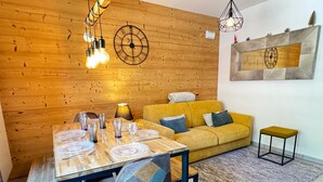 Ein Essbereich mit einem Holztisch, gedeckt für vier Personen, einem gelben Sofa und einem kleinen Hocker.