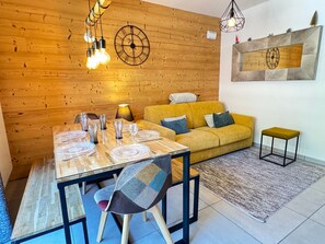 Ein Essbereich mit einem Holztisch, gedeckt für vier Personen, einem gelben Sofa und einem kleinen Hocker.
