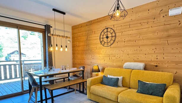 Ein gemütliches Wohnzimmer mit gelber Couch, einer Holzwand und einem Essbereich mit Tisch und Stühlen.
