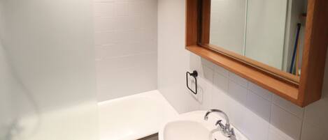 A bathroom with a white bathtub, a wooden-framed mirror, and white tiled walls.