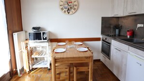 A small kitchen with a wooden table set for two, a clock on the wall, and basic appliances. - Studio with terrace and garage in Les Gets (Les Gets)