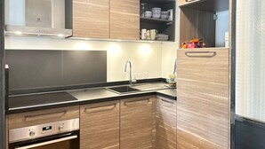 A modern kitchen with wooden cabinets, a stainless steel range hood, and a built-in oven. - Modern Stylish Studio with Spa Access, Central Location, Close to Slopes (Les Gets)