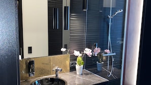 Un baño moderno con un lavabo negro, toallas blancas, cabina de ducha de cristal y una orquídea en maceta.
