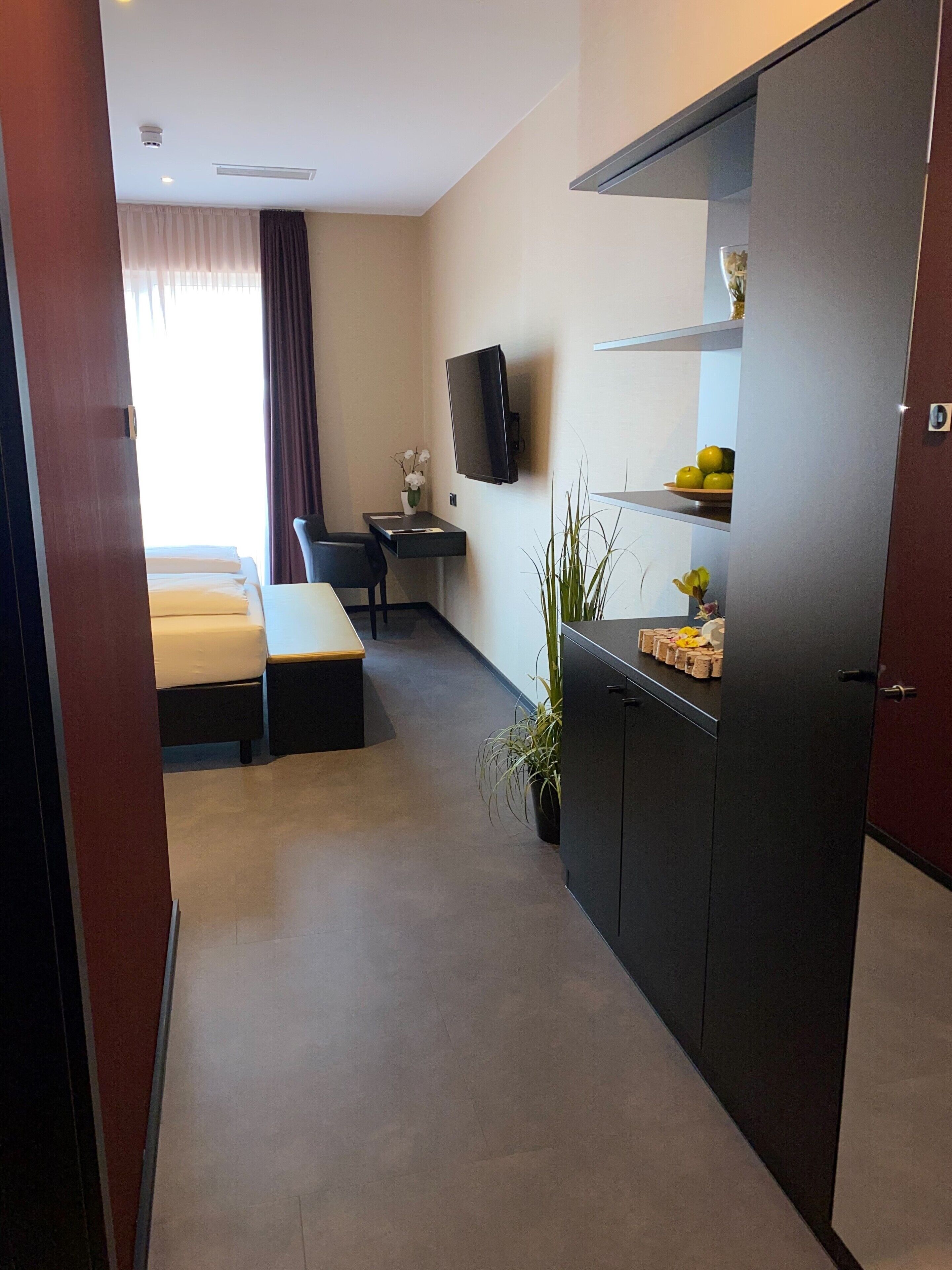 Una habitación de hotel moderna con cama, escritorio, televisión y una pequeña kitchenette.