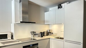 Una cocina moderna con armarios blancos, horno empotrado, microondas, cafetera y escurreplatos.