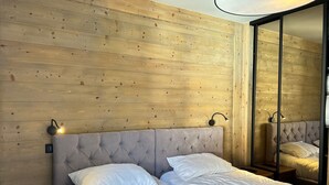 Un dormitorio con cabecera capitonada, una cama grande con ropa de cama blanca y una pared de madera con un espejo.