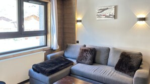 Una sala de estar moderna con un sofá gris, dos almohadones de piel, un control remoto sobre una mesa de centro de madera y una araña.