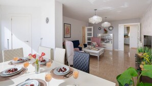 Una sala moderna con comedor, una cocina al fondo y una araña.
