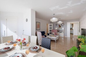 A modern living room with a dining area, a kitchen in the background, and a chandelier. - Fidalsa Bella Vista junto al mar (El Campello)
