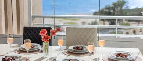 Una mesa lista para comer con vista al océano, un florero con flores y un plato de comida.