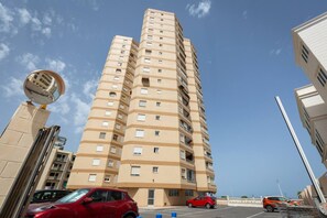 A high-rise building with multiple floors, a parking area with cars, and a clear sky. - Fidalsa Bella Vista junto al mar (El Campello)