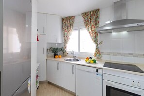 A modern kitchen with white cabinets, a stainless steel sink, a stove, and a window with floral curtains.