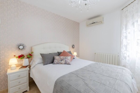 A bedroom with a bed, bedside tables, lamps, and an air conditioning unit.