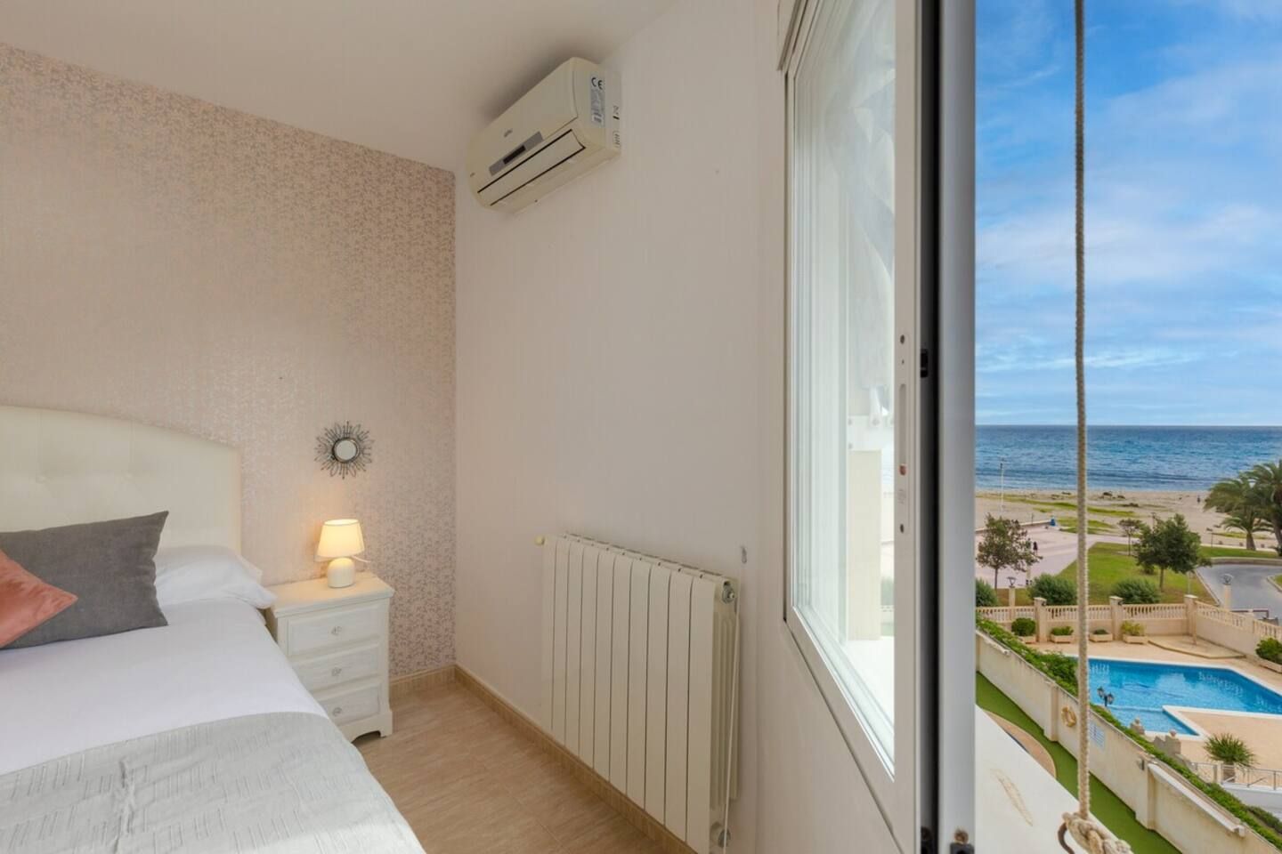Ein Schlafzimmer mit Bett, Nachttischlampe und Blick auf Strand und Pool.