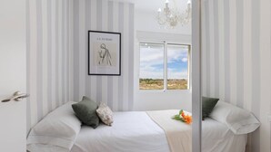Un dormitorio con cama, almohadas, un cuadro enmarcado en la pared y una ventana con vistas.