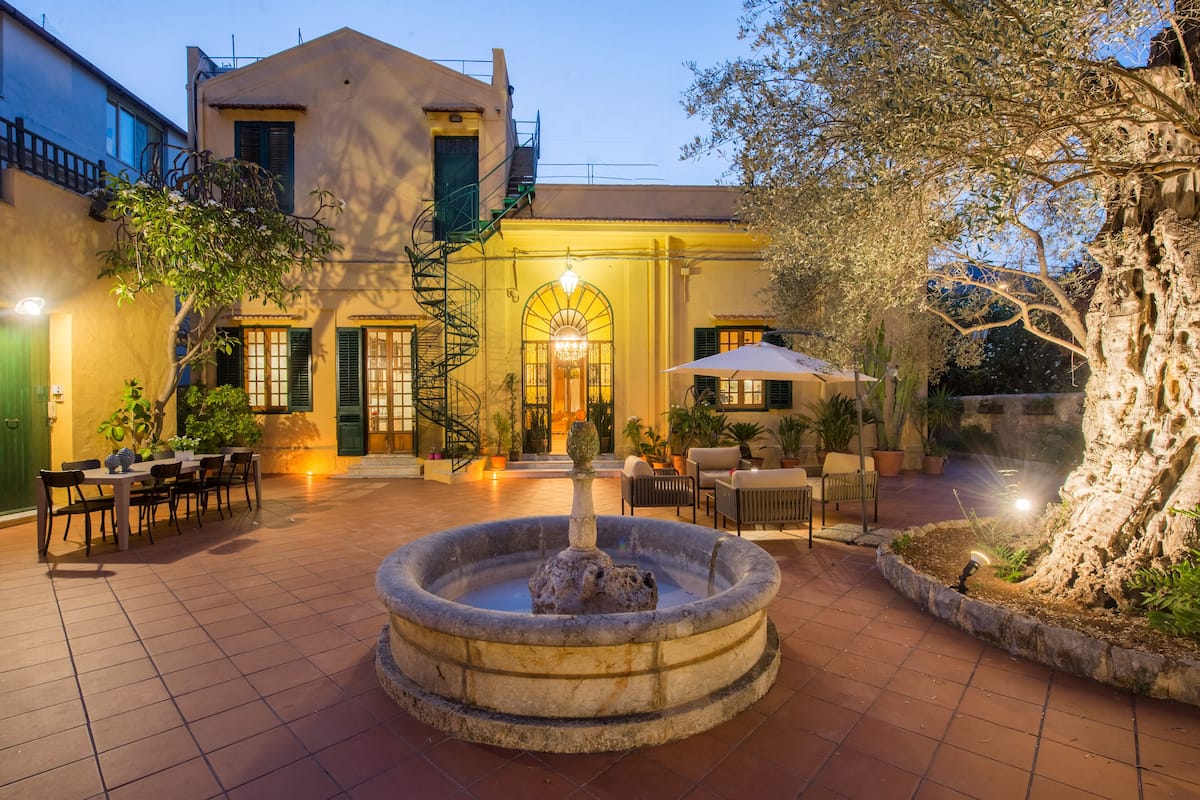A courtyard with a fountain, outdoor seating, and a staircase leading to the entrance.