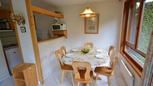 A dining area with a round table, wooden chairs, a bowl, and a hanging light fixture. - Ski-In/Ski-Out Apartment in Les Gets - 3 Stars, Balcony, Mountain Views, Free Shuttle (Les Gets)