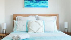 Una cama bien tendida con una colcha azul y blanca, un almohadón blanco con detalles azules y un cojín decorativo con diseño de diamantes.