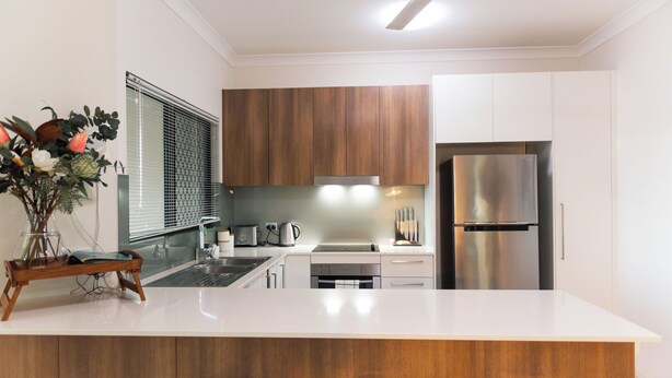 Una cocina moderna con encimeras blancas, armarios de madera y electrodomésticos de acero inoxidable, además de una isla central.