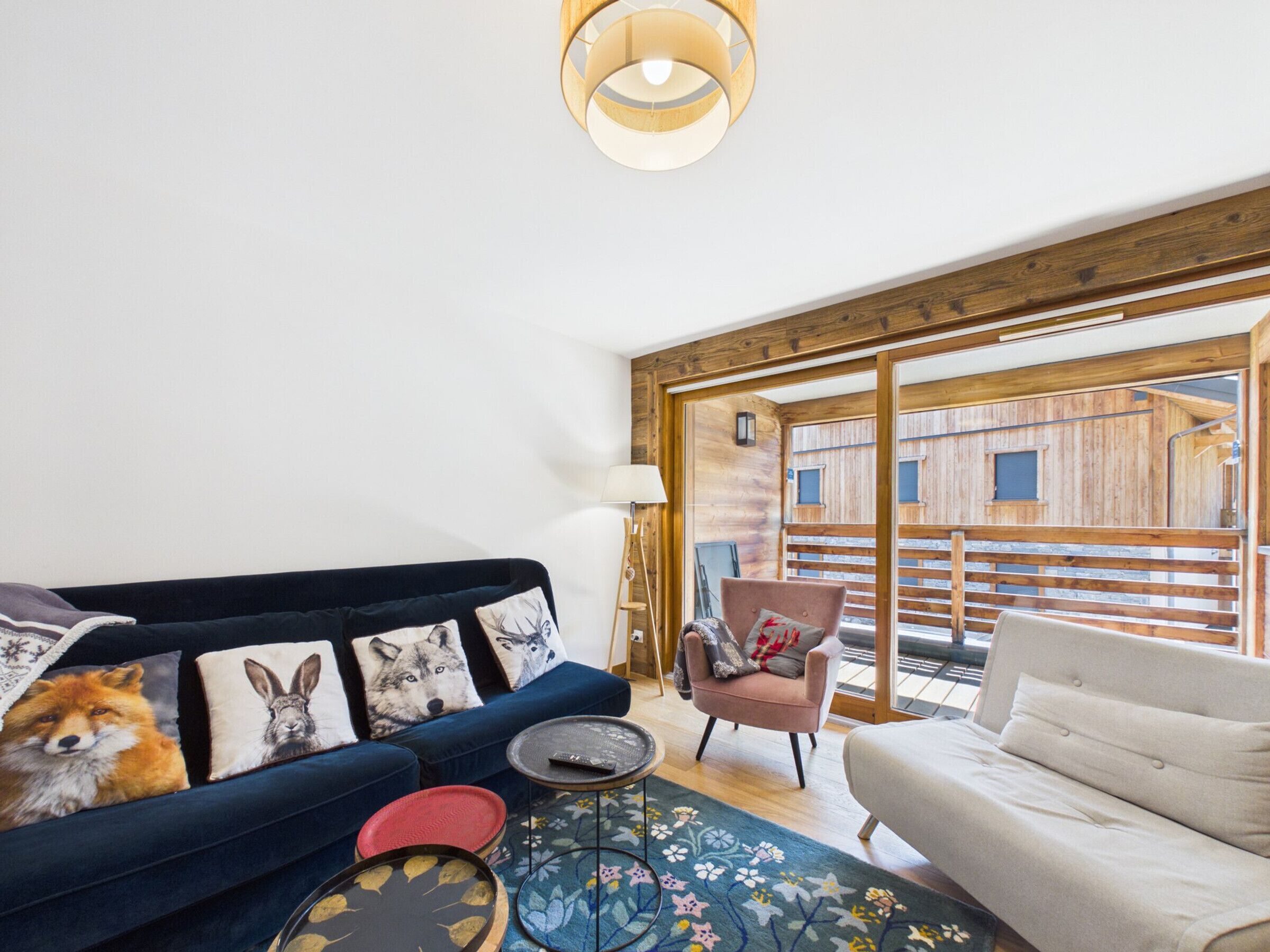 Una sala de estar moderna con un sofá azul, un sillón blanco y un ventanal con marco de madera que da a una terraza de madera.