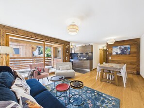 A modern living room with a sofa, a coffee table, and a dining area with a table and chairs. - Luxury Apartment in Central Les Gets with Parking and Balcony (Les Gets)