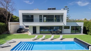 Une maison moderne à deux étages, dotée d’une piscine, d’un patio couvert et d’une voiture garée à l’extérieur.