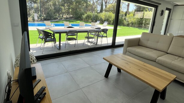 Un salon moderne doté d’une grande porte-fenêtre coulissante donnant sur une terrasse extérieure avec une piscine et des chaises.