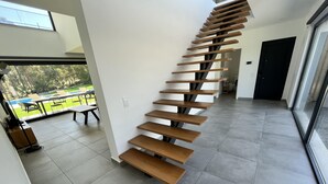 Un escalier moderne avec des marches en bois et une rampe en verre, menant à un espace extérieur aménagé avec une table et des chaises.