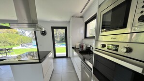 Une cuisine moderne avec des meubles blancs, des appareils en acier inoxydable et une vue sur une piscine et un jardin.