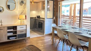 Eine moderne Küche mit Holzausstattung, einem Essbereich mit Tisch und Stühlen sowie einem großen Fenster mit Blick auf einen Balkon.