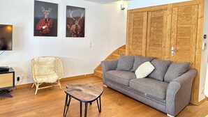 Ein modernes Wohnzimmer mit grauem Sofa, Holzboden, Weidenkorbstuhl und zwei an der Wand befestigten Bildern.