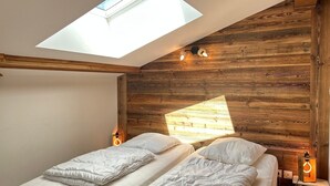 Ein Schlafzimmer mit zwei Betten, einem Oberlicht, Holzwänden und einem kleinen Tisch mit einer Lampe.