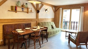 A cozy room with a wooden dining table set for four, a sofa, and a window with a view.