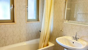 A bathroom with a bathtub, a sink, a window, and a mirror.