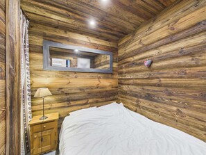 A bedroom with wooden walls, a bed, a nightstand, a lamp, and a mirror.