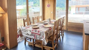 A wooden dining room with a table set for six, large windows, and a view of a mountainous landscape.