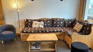 A cozy living area with a sofa, a small table, and a chair. There are two wall-mounted lamps and a window with a view.
