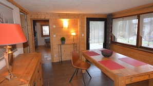 Un interior de madera con una mesa de comedor, sillas, una lámpara y una ventana con cortinas.