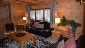 Interior acogedor de una cabaña de madera con sofá, dos lámparas, una mesita de centro y una planta en maceta.