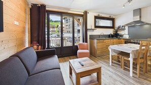 Ein kompakter Wohnbereich mit einer Couch, einem kleinen Tisch, einer Küchenzeile mit Herd und Spüle sowie einem Balkon mit Blick auf Gebäude.