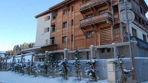 Un edificio de madera de varios pisos con balcones, suelo cubierto de nieve y cielo despejado.