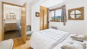 Un dormitorio con una cama grande, una ventana con vistas, una puerta de madera y un baño visible a través de una puerta abierta.