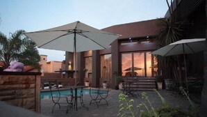 Un patio moderno al aire libre con piscina, sombrillas y mobiliario.