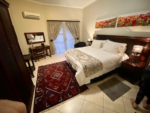 Habitación de hotel con cama, escritorio, silla, lámpara de escritorio, mesita de noche con lámpara y ventana con cortinas.