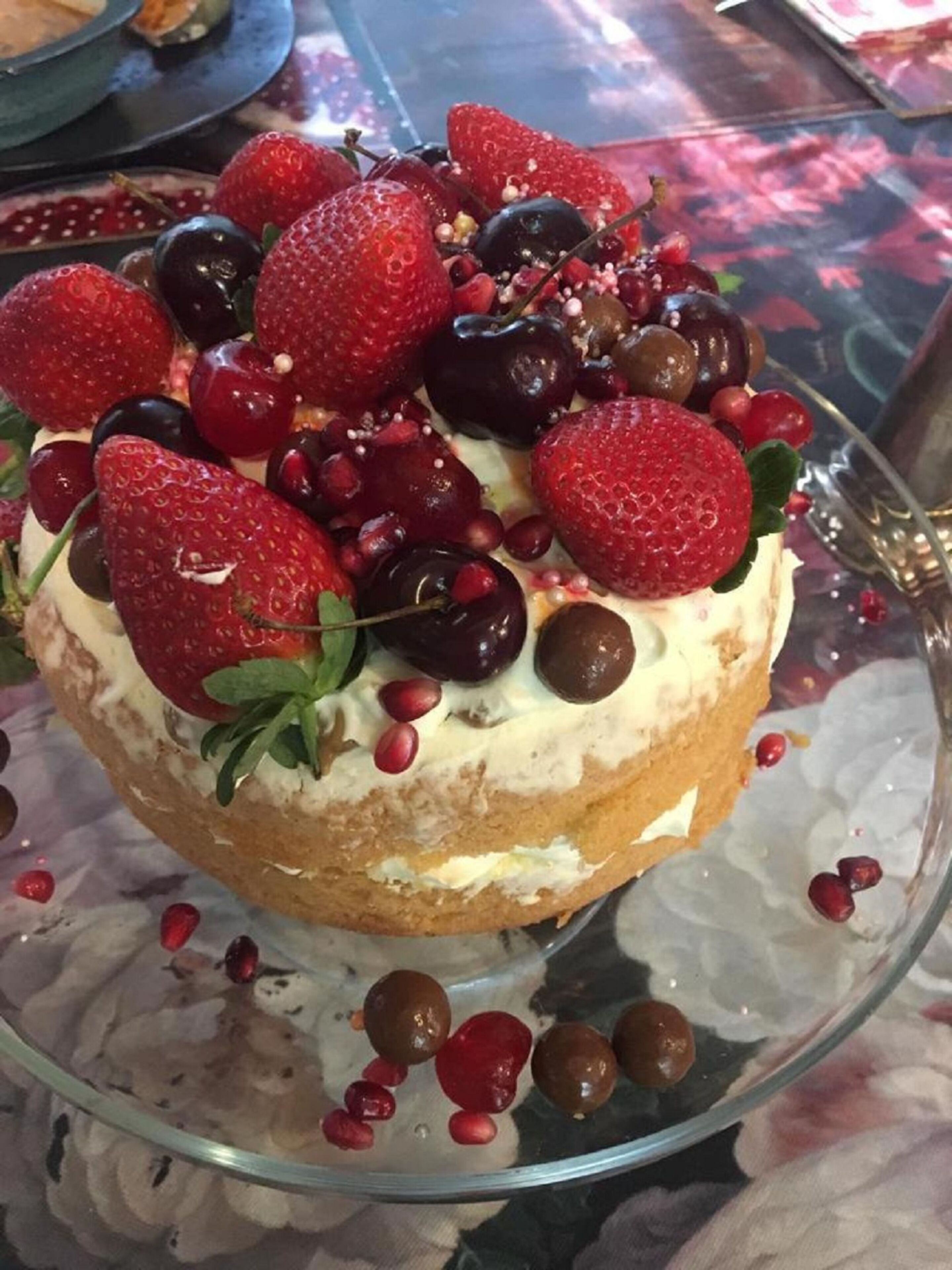 Un pastel con fresas, cerezas y semillas de granada sobre un plato de vidrio.